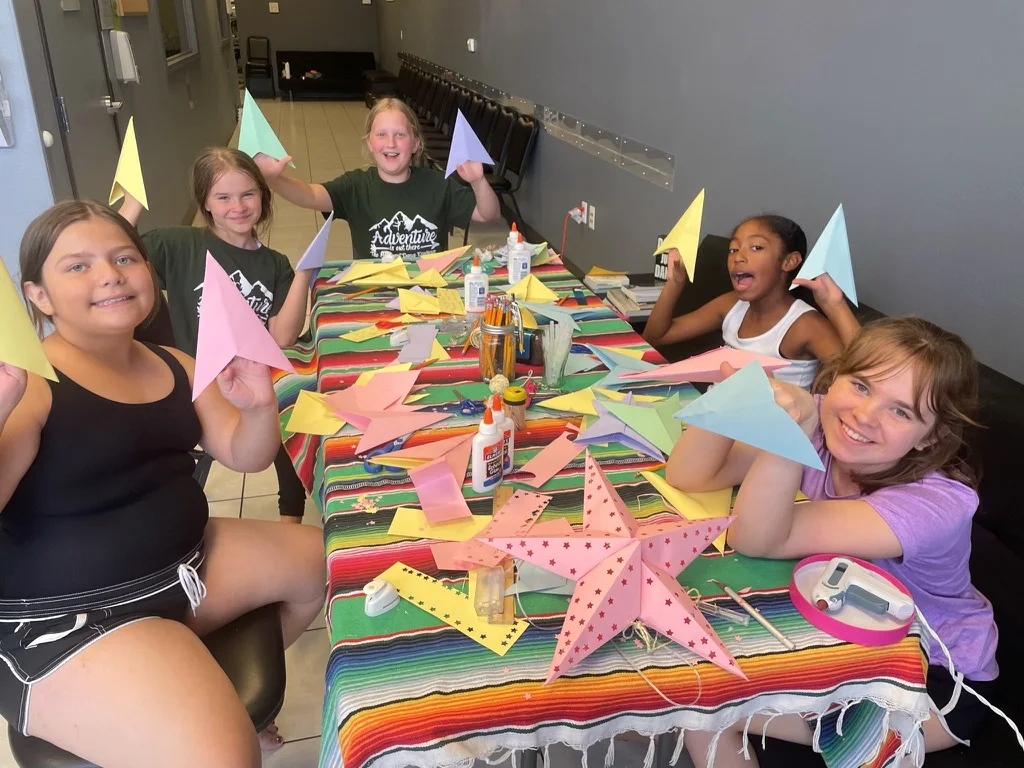 Kids holding up their paper star crafts at a colorful ArtHaus table
