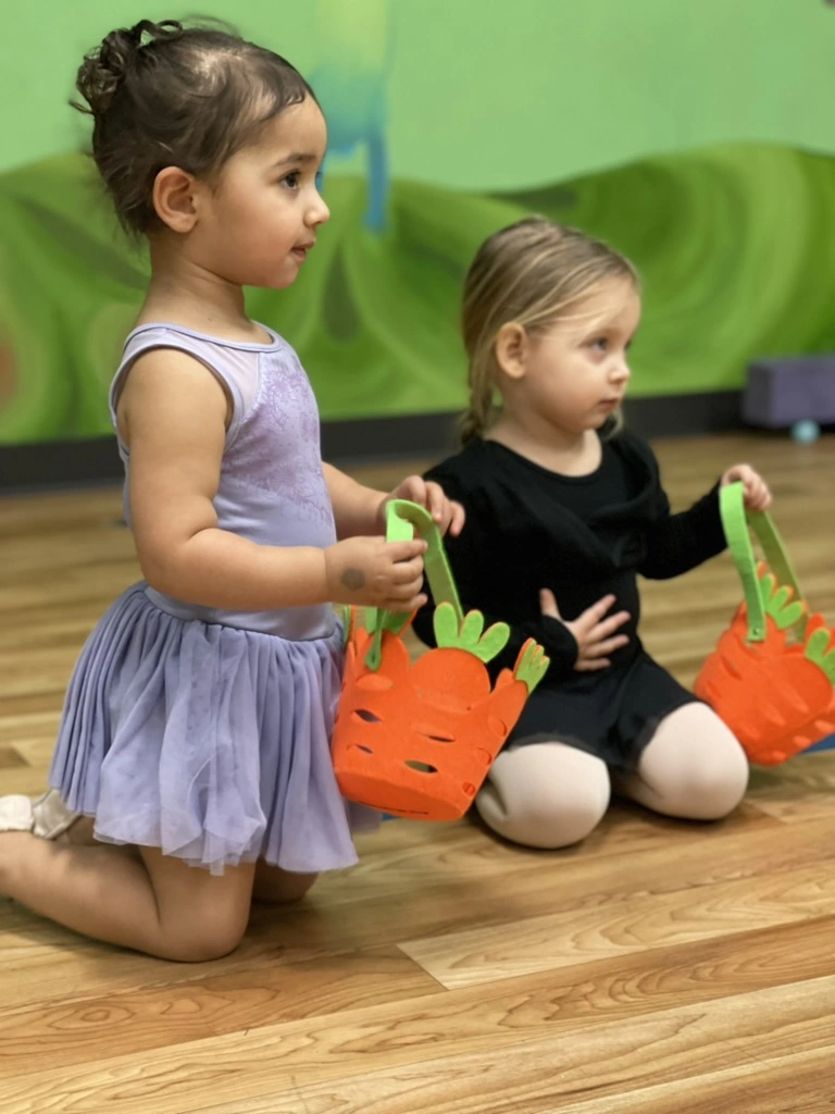 Two toddlers holding carrot baskets in a spring dance class