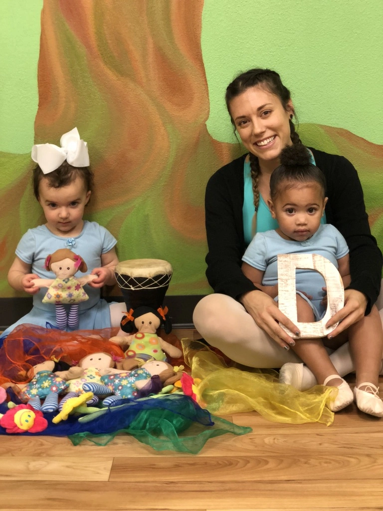A Bravo Babies teacher with two toddlers, dolls, a drum and colorful scarves in class