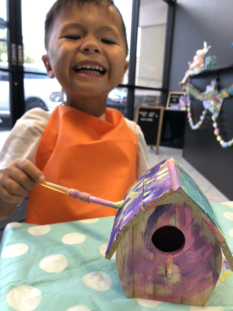 A grinning camper painting his birdhouse