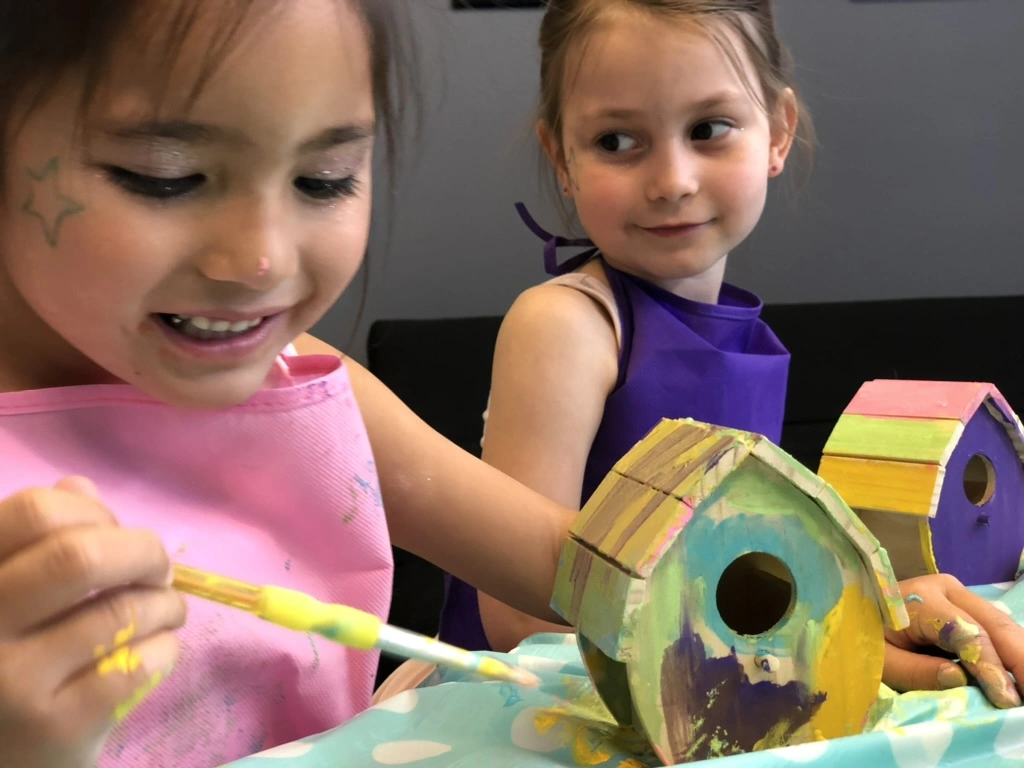 Two campers painting wooden birdhouses