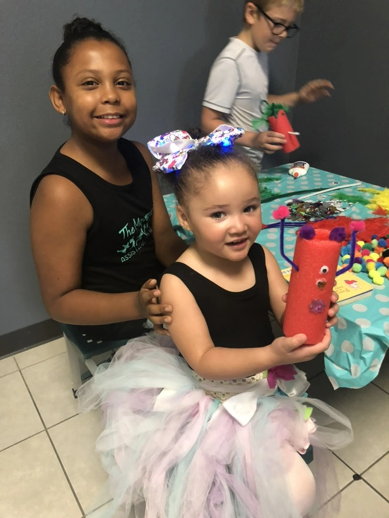 A camper and her helper showing off a pool-noodle craft