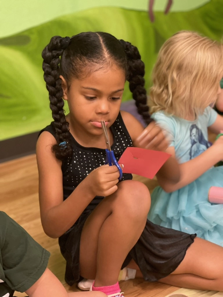 A focused camper cutting a red paper craft