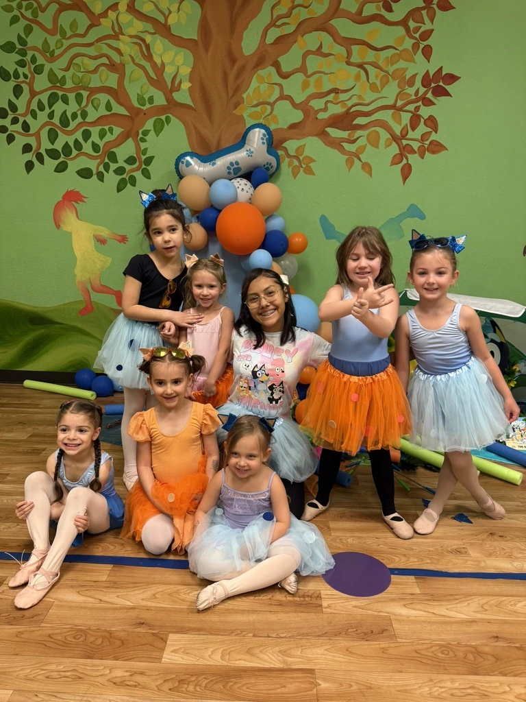 Summer campers in tutus celebrating together in front of a balloon arch