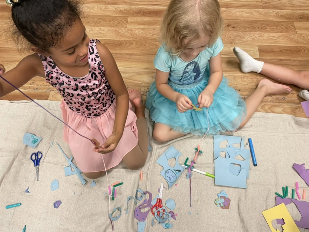 Two summer campers threading yarn crafts on the studio floor