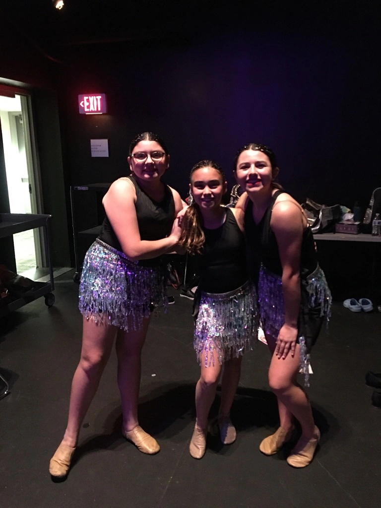 Three company dancers in sequin skirts backstage