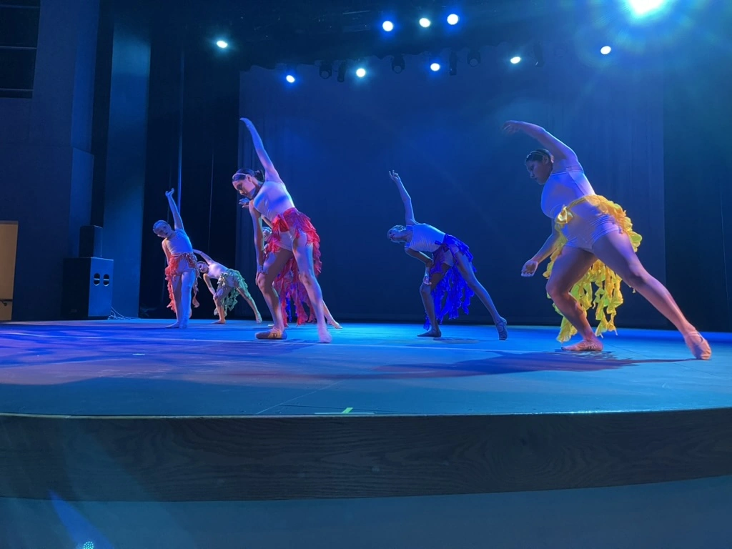 Company dancers in bright ruffled skirts reaching in a deep side stretch on stage