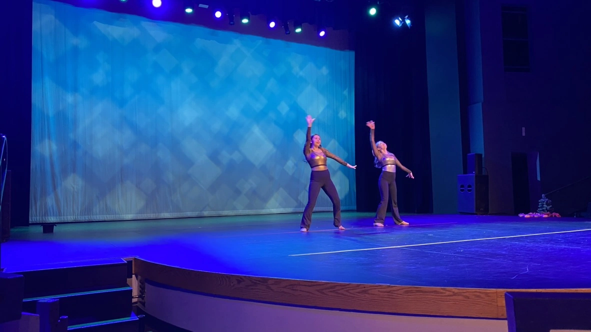 Two company dancers in gold tops kicking in unison