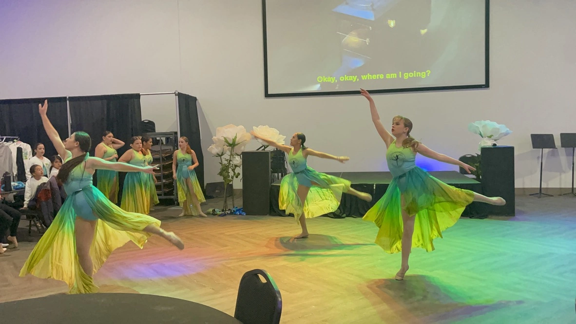 Company dancers in green and yellow ombre dresses performing lyrical