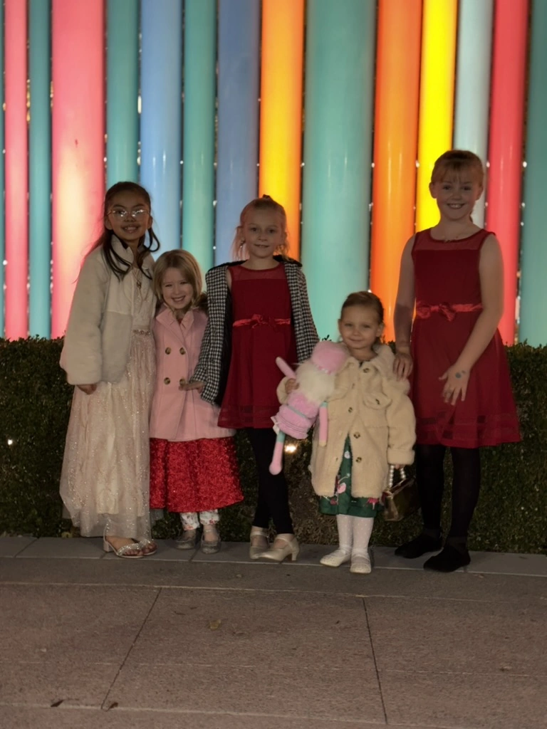 Movement dancers dressed up for a holiday night out in front of colorful lights