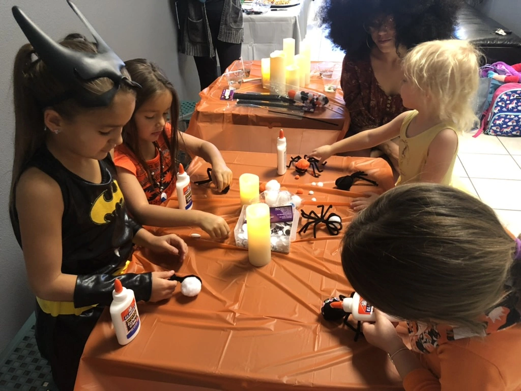 Kids gluing pom-pom spiders at a Movement Halloween party