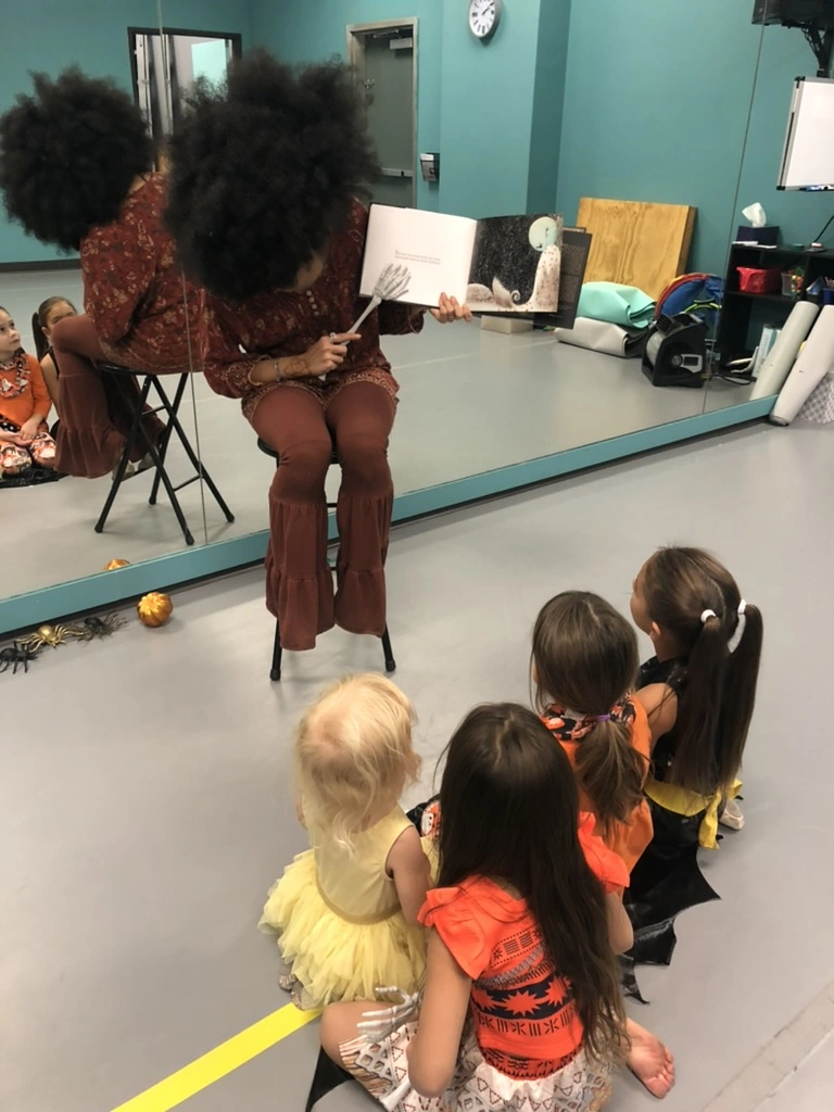 A teacher reading a spooky story to little dancers in costume