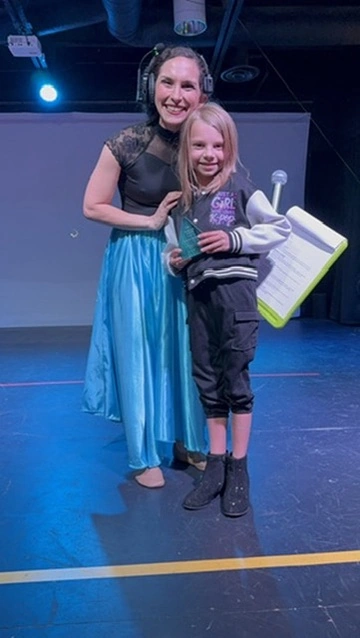 A young dancer holding her award with her teacher after a show at Ovation Theatre