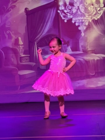 A tiny dancer in a pink tutu striking a pose on stage