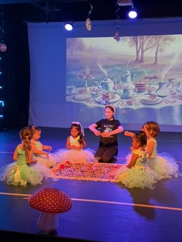 A teacher leads little dancers through a tea party story ballet on stage