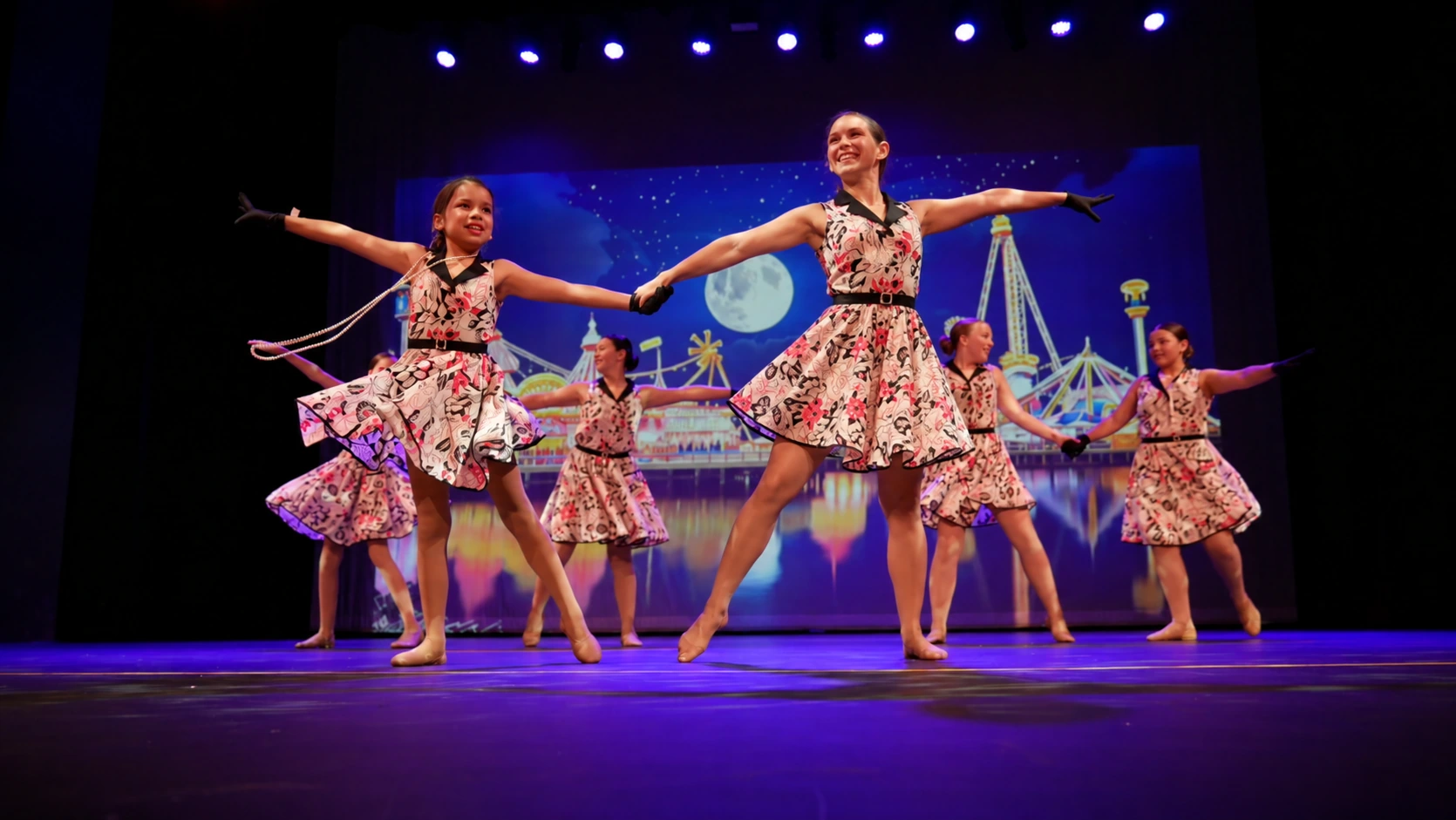 A Movement teacher performing in costume with her students on stage under theatre lights