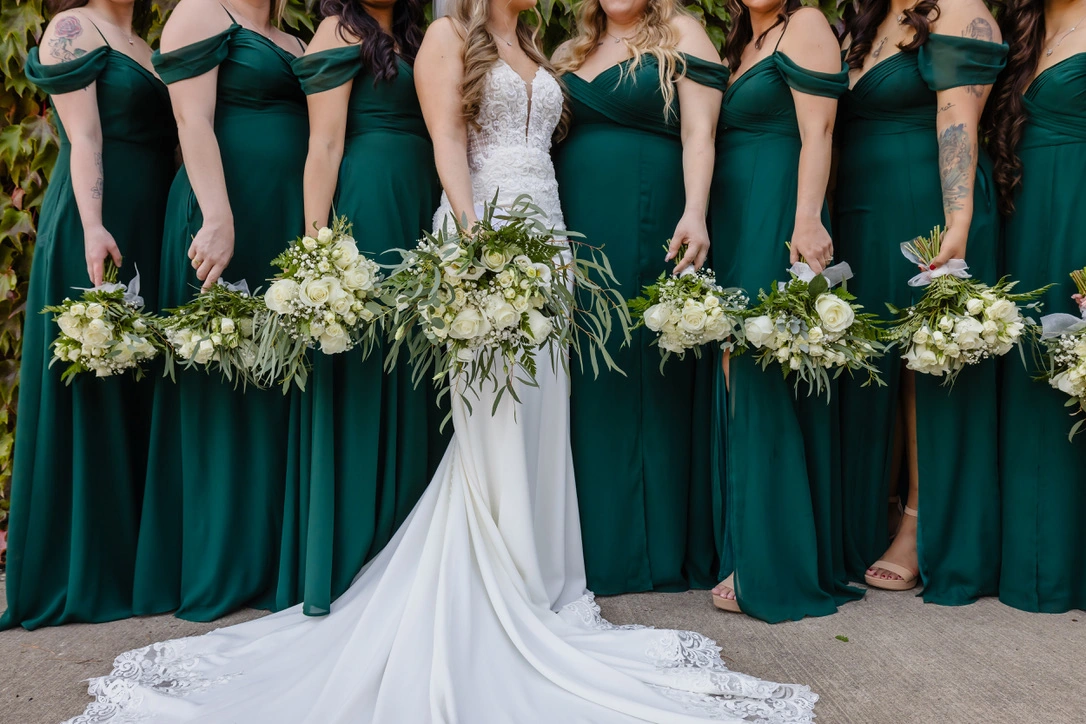 A bride with her bridesmaids in emerald gowns holding white bouquets